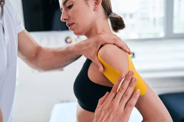 Photo of Unrecognized manual therapist taping yellow tape on patient shoulder in wellness center