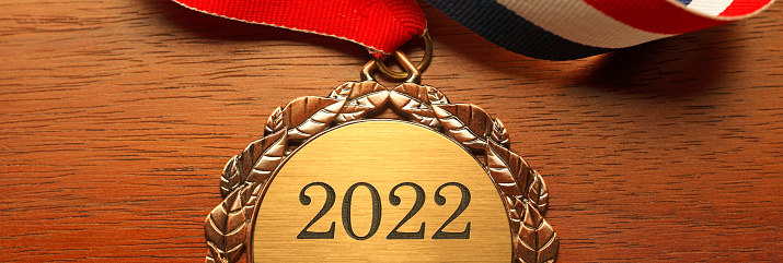 Gold medal engraved with the year 2022 rests on a wood desk.