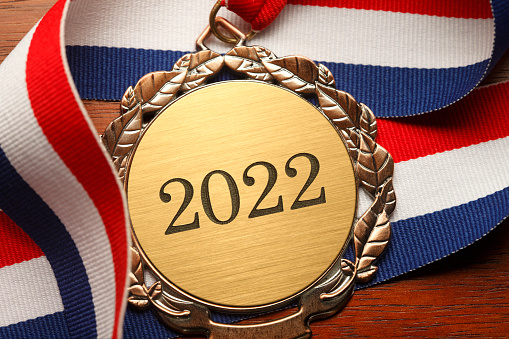 Gold medal engraved with the year 2022 rests on a wood desk.