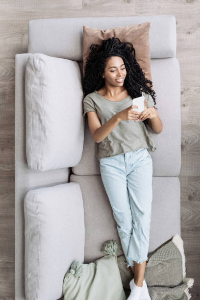 Young woman lying on couch looking at smartphone, relaxing at home