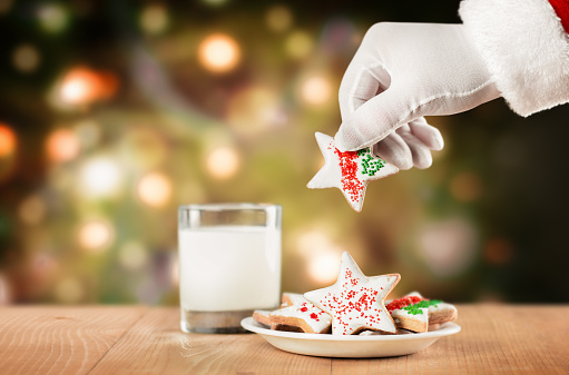 the hand of santa claus takes cookies from a plate on the background of a christmas tree
