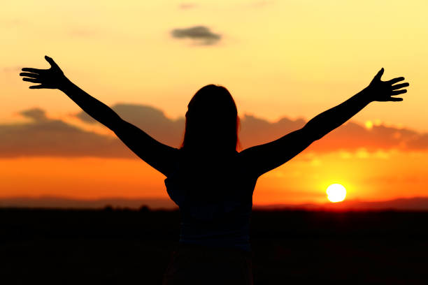 Woman silhouette celebrating stretching arms at sunset