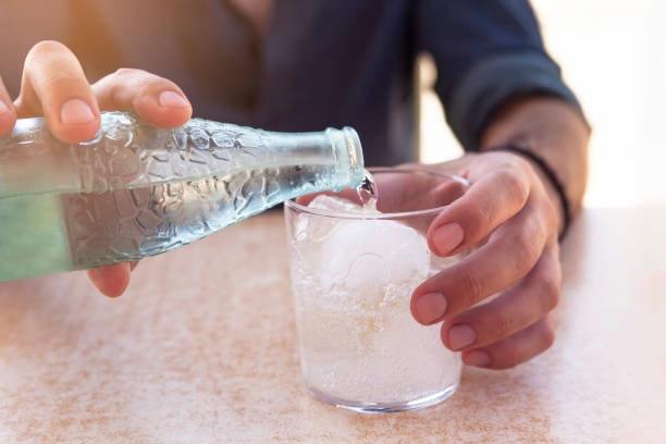 close-up adult man's hand pouring sparkling water into a glass of water outdoors close-up adult man's hand pouring sparkling water into a glass of water outdoors tonic water stock pictures, royalty-free photos & images