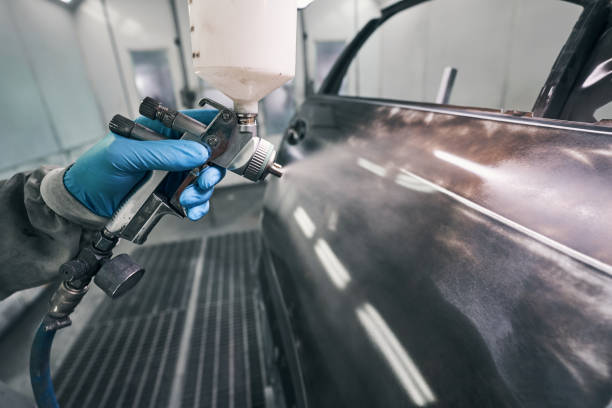 Automobile technician painting auto with spraying gun Mechanic dressed in protective overalls and rubber gloves releasing painting spray from gun to car car bodywork stock pictures, royalty-free photos & images