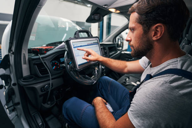 Auto mechanic providing car diagnostics in cabin Male technician clicking on screen of diagnostic tool, attached to steering wheel of a car flat bed scanner stock pictures, royalty-free photos & images