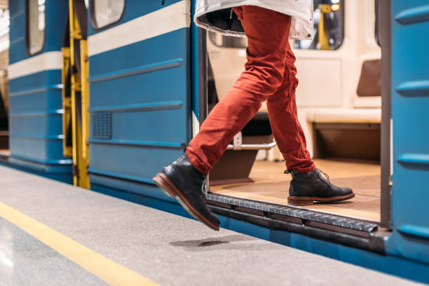 Handsome man in black shoes, burgundy pants and white jacket runs into a subway train. Male is late for work. Selective focus on the left leg. Public transport and mobility in urban concept. Close up. public transportation stock pictures, royalty-free photos & images