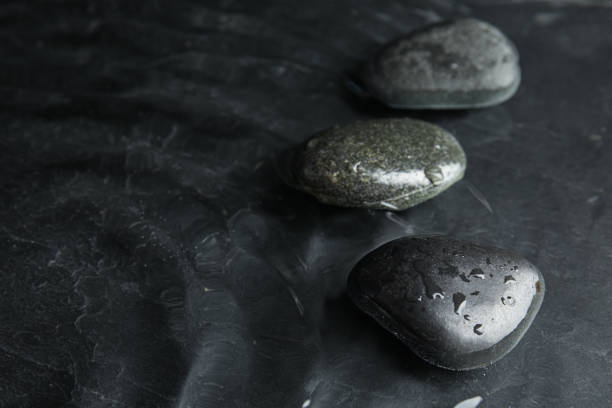 Black zen stones and white orchids on a wooden plank on the surface of the water. SPA, relaxation, meditation concept.