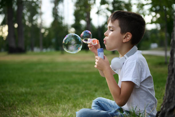 istock Adorable handsome preadolescent child boy blowing starting soap bubbles on the park, resting during his school recreation 1337275834