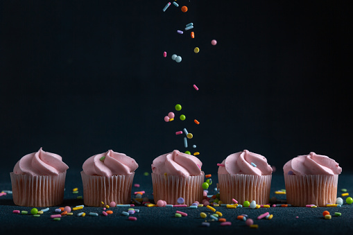 Sprinkles coming down on a line of mini pink cupcakes