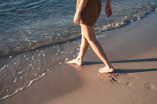 Woman walking barefoot on the beach in the morning at summertime