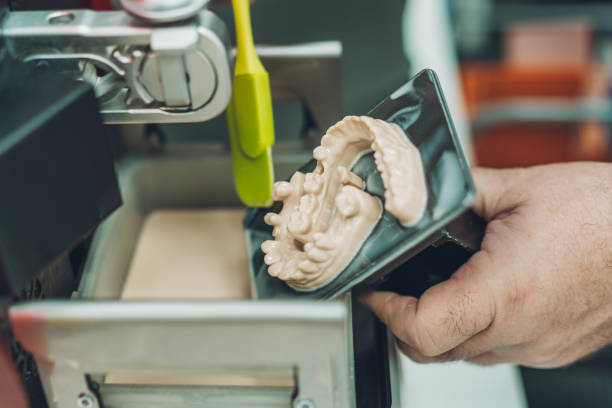 vista de cerca de un hombre que usa una espátula para recoger la resina sobrante de una impresora dental 3d en un laboratorio - technician dentures prosthetic equipment workshop fotografías e imágenes de stock