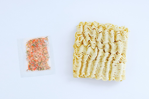 Briquette of dry Asian instant noodles and seasoning for food in a transparent bag on a white background. View from above.