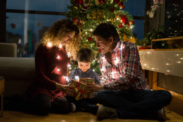 Happy family opening Christmas presents Happy Latin American family at home opening Christmas presents next to the tree and smiling - lifestyle concepts red green and gold christmas trees stock pictures, royalty-free photos & images