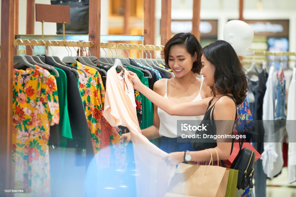 Friends Shopping for Perfect Dres Pretty young female friends shopping for perfect dress in store Shopping Stock Photo