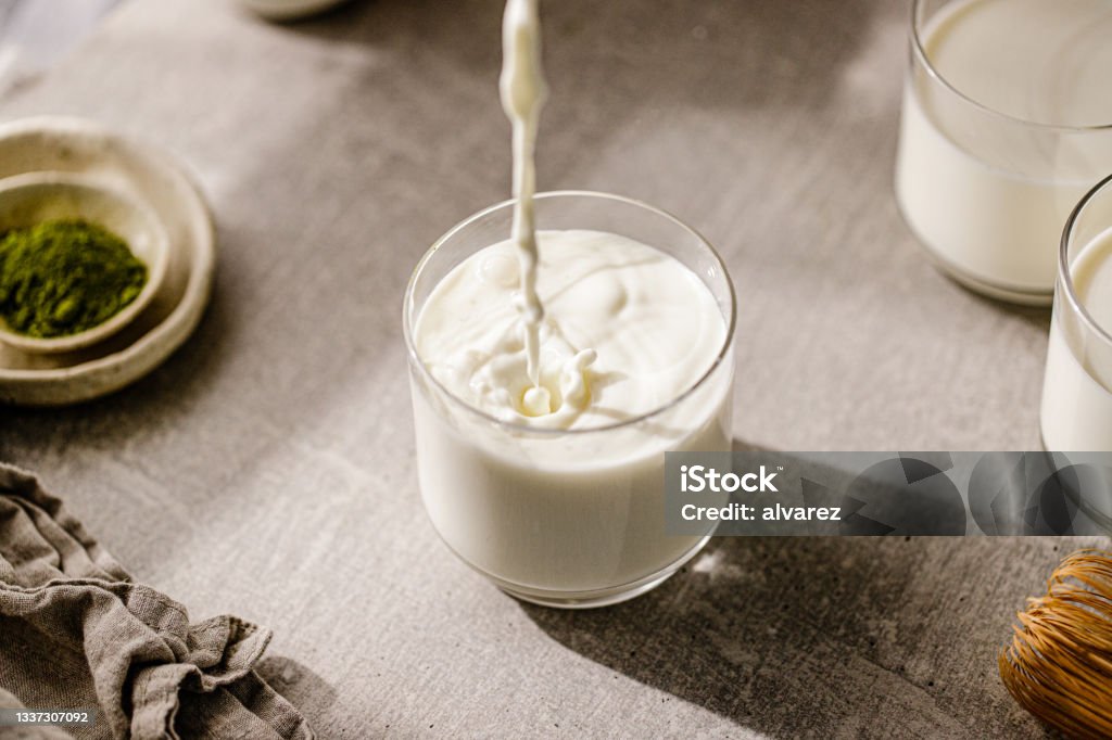 Pouring fresh milk in glass Close-up of pouring fresh milk in glass. Milk is being poured in a glass on the kitchen table at home. Milk Stock Photo