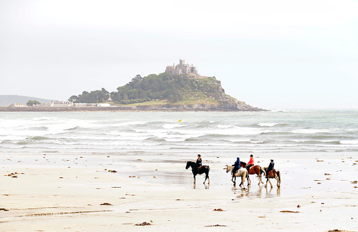 Four horses and riders on the beach in Mounts bay cornwall UK. St Michael's mount the small island can be seen in the background through the mist