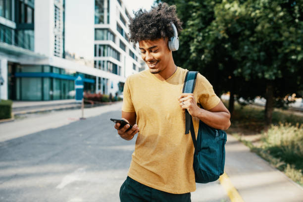 gemischtrassigen millennial-mann in der innenstadt, mit mobiltelefon - kopfhörer stock-fotos und bilder