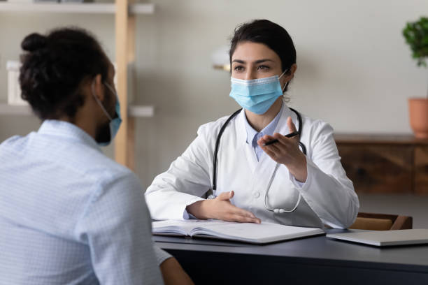 young indian doctor in facemask giving consultation to african patient. - médico geral imagens e fotografias de stock