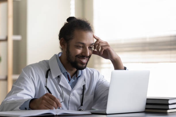 Happy millennial male african american doctor working on computer.