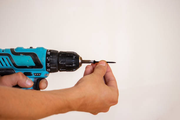 istock Hand with cordless screwdriver and drill isolated on white background. Twists screws into the board. 1337312850