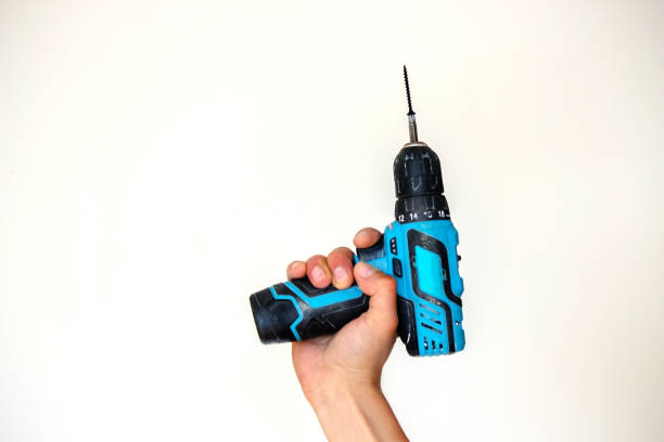 istock Hand with cordless screwdriver and drill isolated on white background. Twists screws into the board. 1337312855