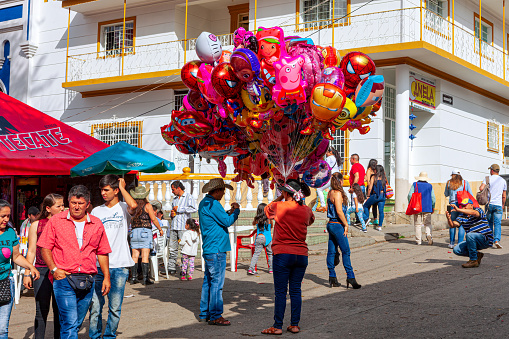 San Francisco, Cundinamarca, Colombia - August 20, 2017: It is Fiesta time in the Cundinamarca town of San Francisco in the Latin American country of Colombia. Local Colombian people are seen walking around the main town square. A couple of balloon sellers are seen with their balloons for sale. The elevation at street level is 4990 feet above mean sea level. Photo shot in the afternoon sunlight; horizontal format.