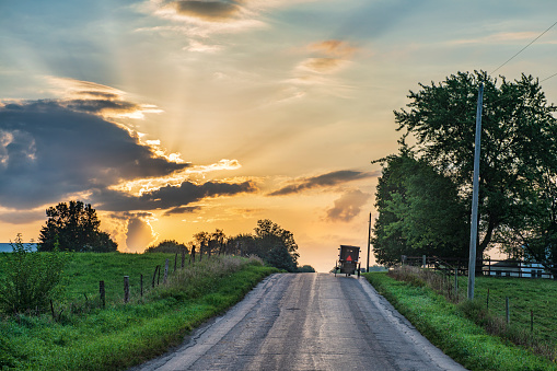 Rural Indiana Road with Amish Buggy and the sun behind the clouds sending sunbeams across the sky.