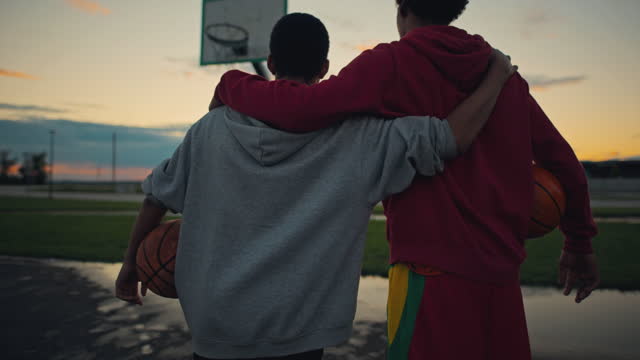 Slow motion shot of a young basketball players embrace each other while they standing on the basketball court at sunset.