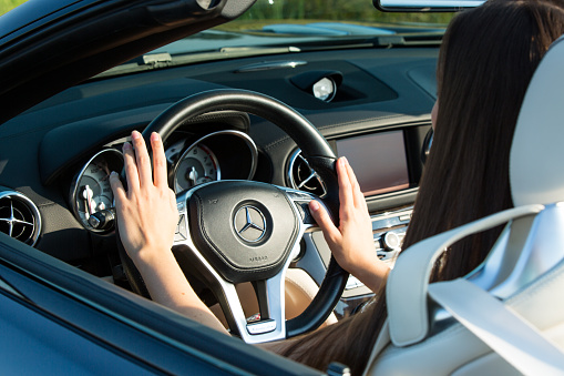Dnepropetrovsk, Ukraine - 08.24.2021: Closeup on female hands driving Mercedes Benz car luxury transportation lifestyle. Mercedes Benz SL550 convertible on the road.