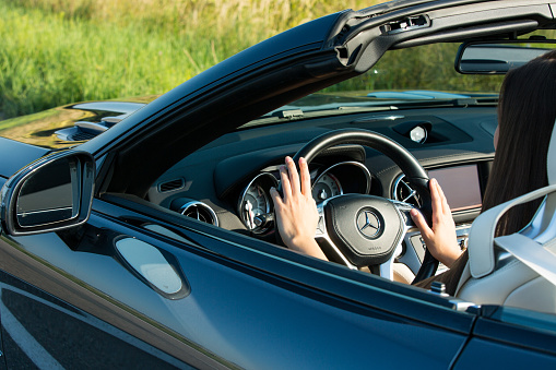 Dnepropetrovsk, Ukraine - 08.24.2021: Closeup on female hands driving Mercedes Benz car luxury transportation lifestyle. Mercedes Benz SL550 convertible on the road.