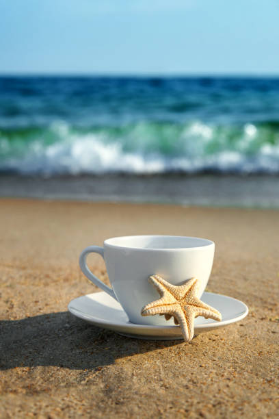 white cup with tea or coffee on sand beach front of sea