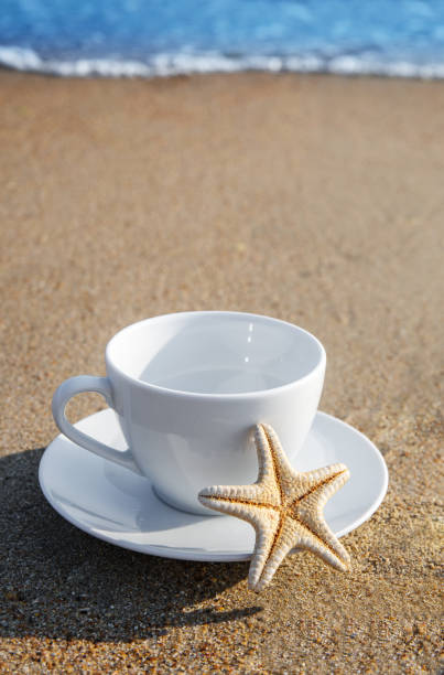 white cup with tea or coffee on sand beach front of sea