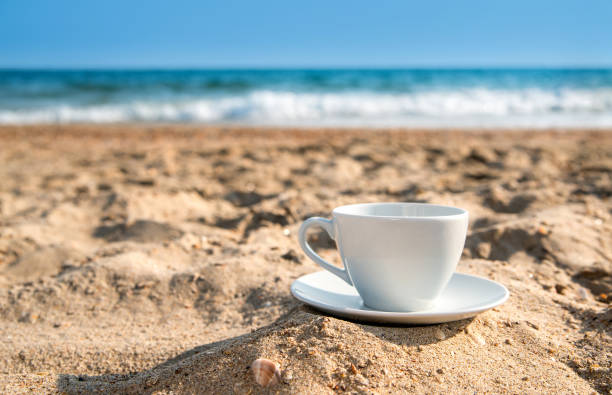 white cup with tea or coffee on sand beach front of sea