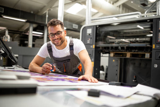istock Print house worker controlling printing process quality and checking colors with magnifying glass. 1337327256