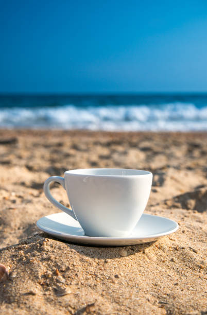 white cup with tea or coffee on sand beach front of sea