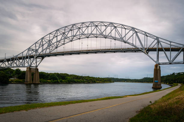 istock Sagamore Bridge over Cape Cod Canal and bikeways along the riverbank. Dramatic cloudscape over the arching bridge over the river. 1337328201
