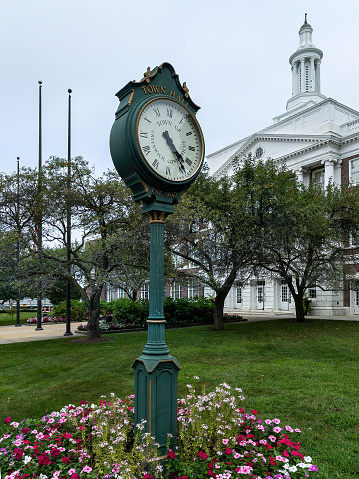 Greenwich, CT - USA - Aug. 29, 2021: Vertical image of a historic street clock in front of the iconic Greenwich Town Hall.