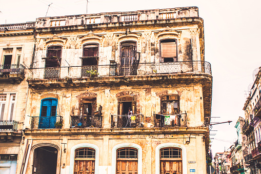 Havana, Cuba - July 06 2018 : No money to take care of this colonial era buildings at the corner of a street. People hanging out of the window