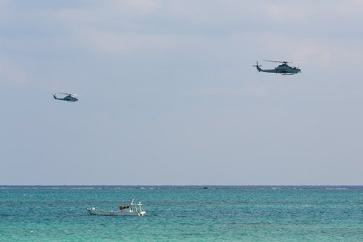 A couple of US Military Bell AH-1 Cobra helicopters patrolling low over ocean waters on a sunny day in Okinawa, Japan