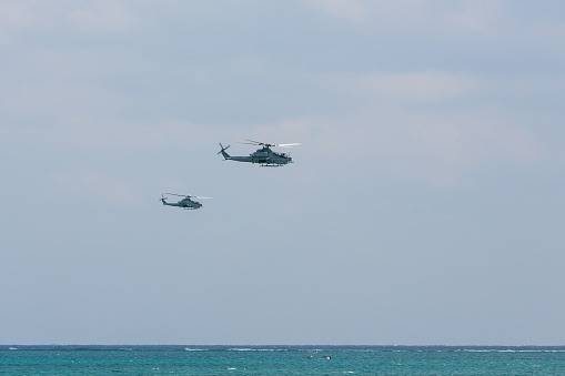 A couple of US Military Bell AH-1 Cobra helicopters patrolling low over ocean waters on a sunny day in Okinawa, Japan