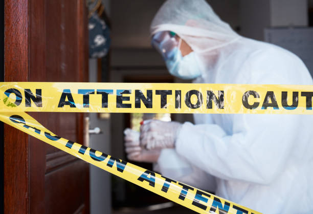 Closeup shot of barrier tape across a doorway with a worker in a protective suit in the background Barricading a hazardous site biohazard cleanup stock pictures, royalty-free photos & images