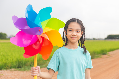 Asian child girl with pinwheels, little girl in summer day holds windmill in hand, Happy kid playing outdoors