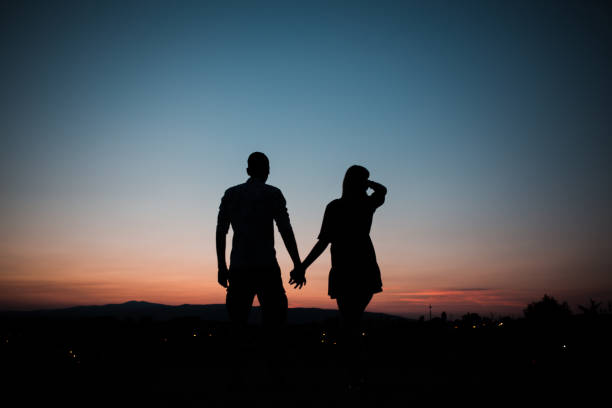 jeune couple amoureux se tenant la main et regardant le coucher du soleil - attractive couple photos et images de collection