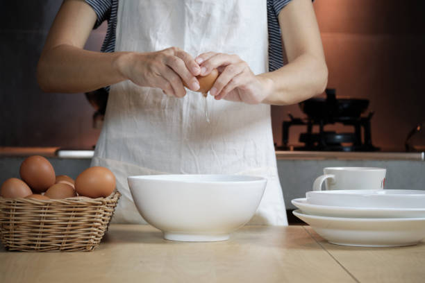 istock Female cook in a white apron is cracking an egg in home's kitchen. 1337355344