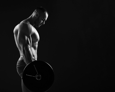 Strong men athlete, weightlifter does exercises, feeling strong tension in muscles during working out with barbell over background with copy space. Side view. Young man lifting weights