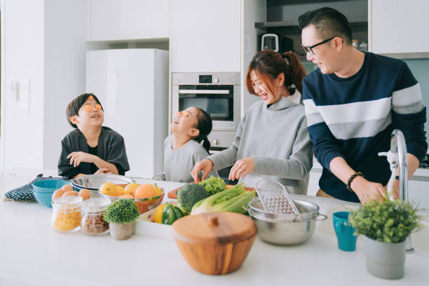 игривая азиатская китайская молодая семья с 2 детьми готовит еду на кухне, наслаждаясь веселым временем вместе - chinese ethnicity family togetherness happiness стоковые фото и изображения