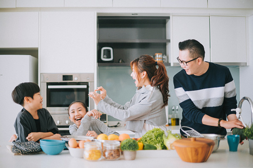 playful asian chinese young family with 2 children preparing food in kitchen enjoying fun time together