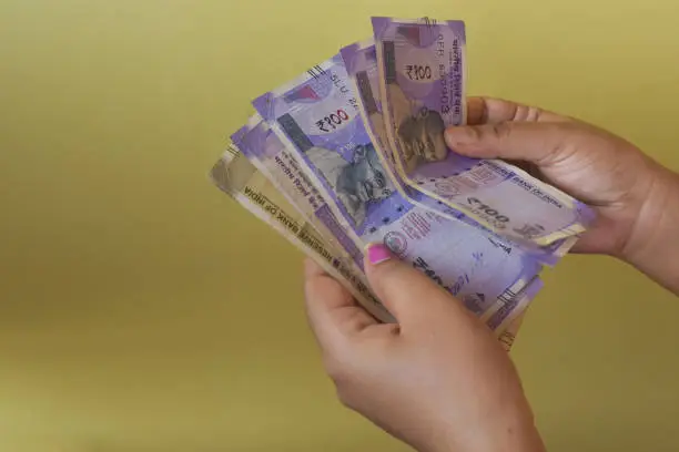 Female hands holding Indian rupee banknotes on a yellow background. Money in woman's hand concept.