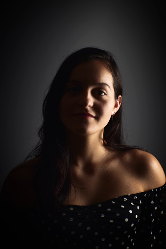 Close-up portrait of a young woman with a positive gaze looking at the camera, on a dark studio background. Happiness concept