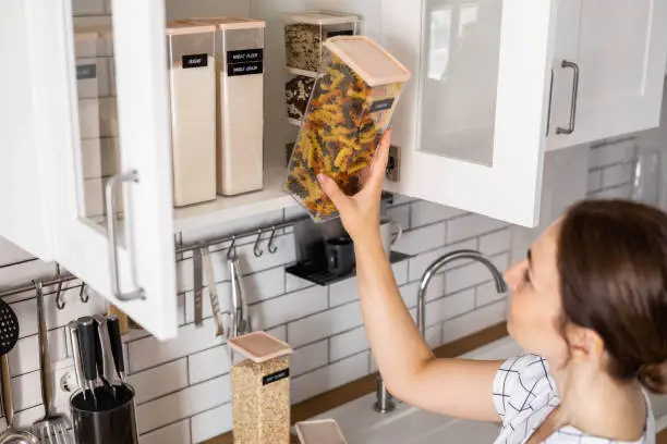 Photo of Laughing young female housewife posing during general cleaning, tidying up in cupboard kitchen